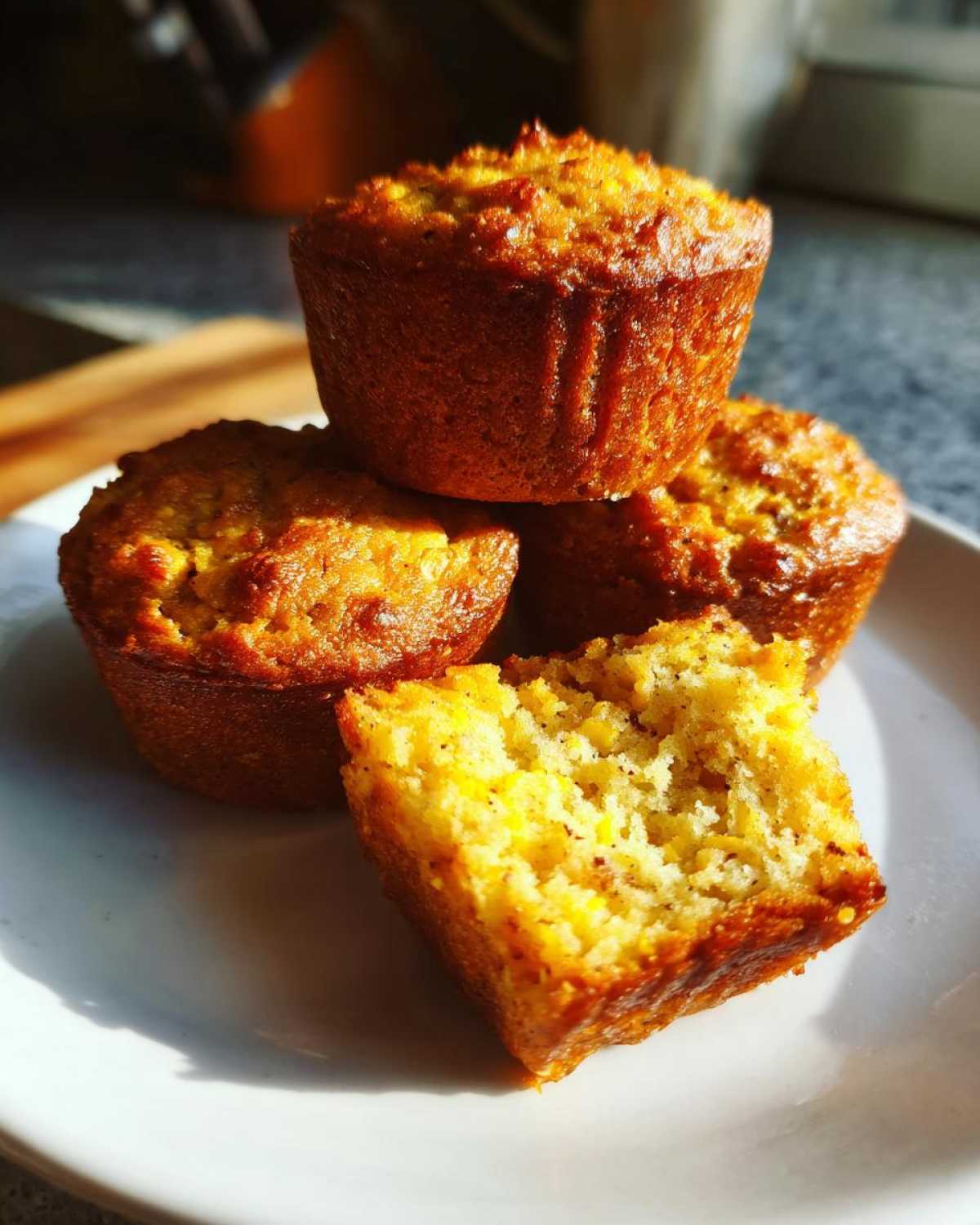 A stack of four golden-brown banana protein muffins, with one cut open to show the moist, yellow interior.