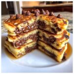 A stack of fluffy chocolate chip pancakes cut in half, revealing gooey melted chocolate filling and topped with chocolate chips.