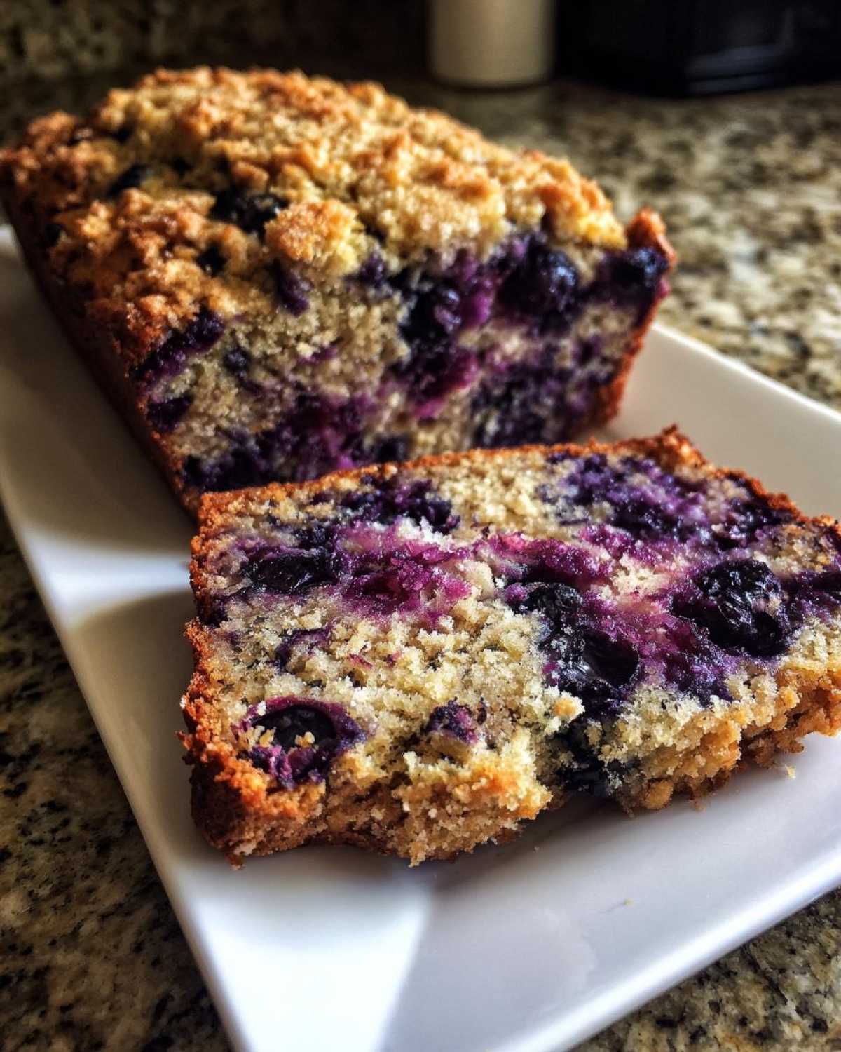 A slice cut from a loaf of moist blueberry banana bread featuring a golden crumb topping.