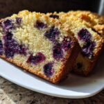 Two thick slices of moist blueberry banana bread showing rich purple blueberries embedded in the golden crumb.