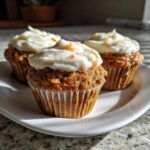 Three delicious carrot cake muffins topped with thick cream cheese frosting and carrot zest.