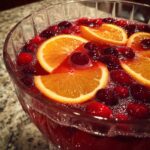 Close-up of a fizzy champagne punch garnished with bright orange slices and whole cranberries.