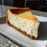 Close-up of a perfect slice of creamy cheesecake recipe with a golden top and graham cracker crust.