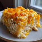 A close-up slice of cheesy chicken and rice casserole topped with melted cheddar cheese.