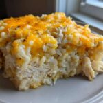 A close-up serving of cheesy chicken and rice casserole topped with melted cheddar cheese.