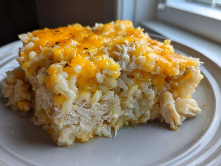 A close-up serving of cheesy chicken and rice casserole topped with melted cheddar cheese.