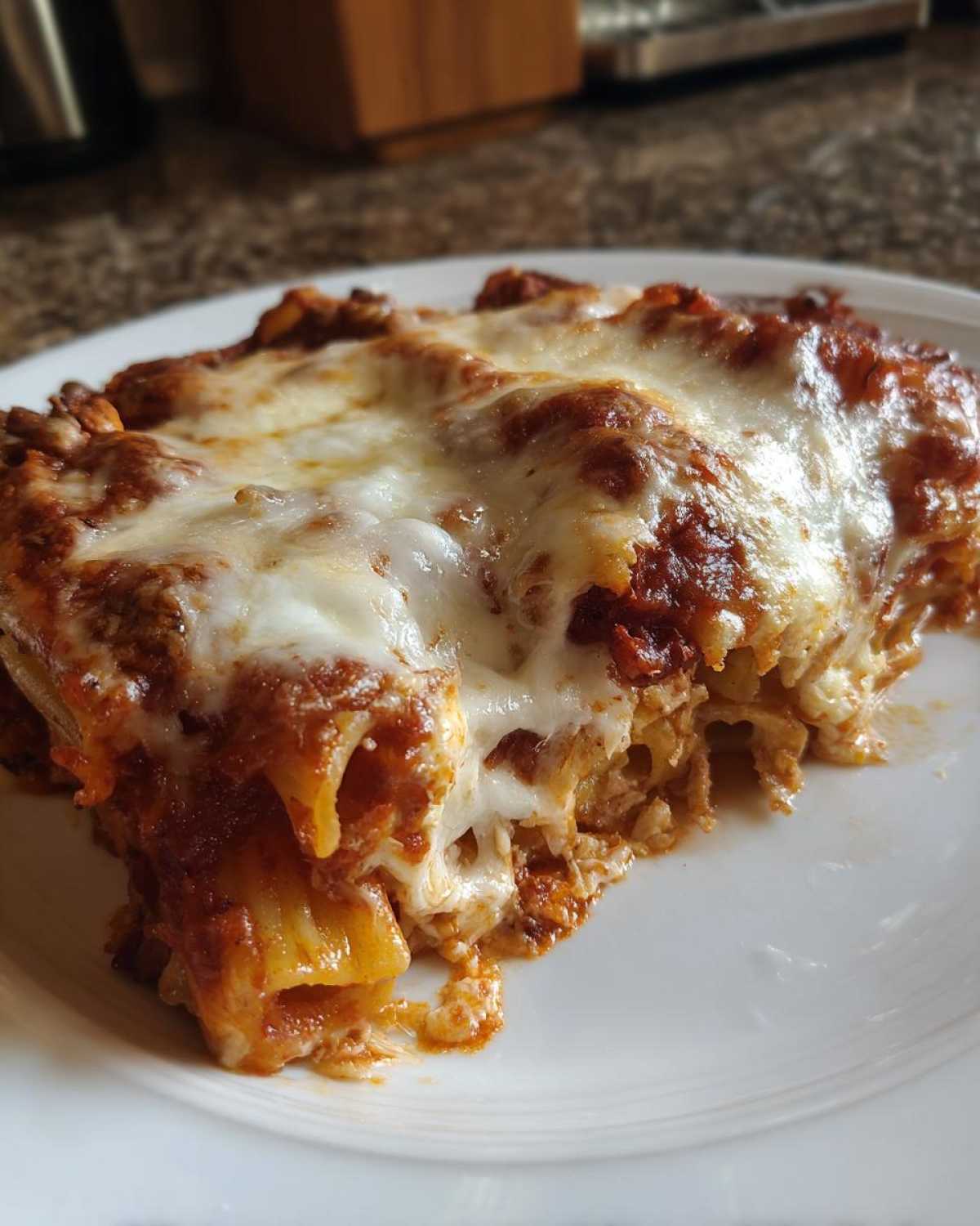 Close-up of a generous serving of cheesy pasta bake topped with gooey, melted mozzarella cheese.