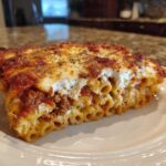 A generous slice of cheesy pasta bake featuring ziti noodles, meat sauce, and a thick layer of melted cheese topping.