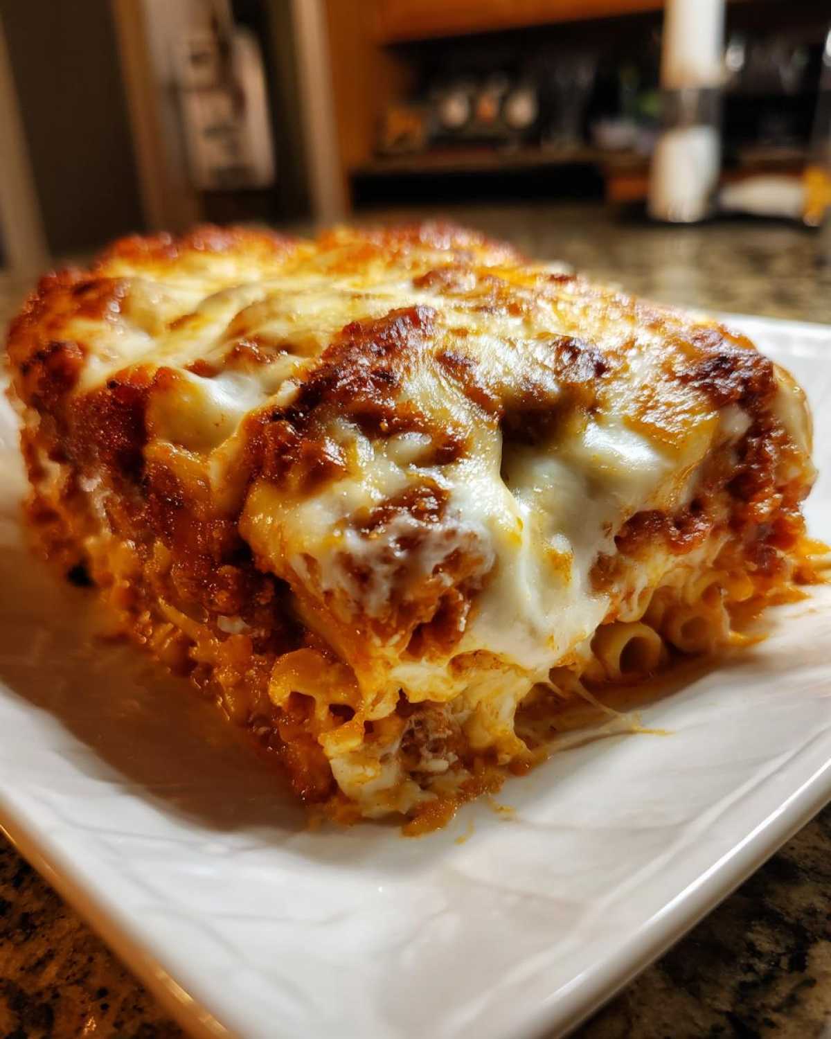 A close-up of a thick, cheesy slice of pasta bake with bubbling, browned mozzarella on top.