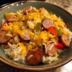 Close-up of cheesy sausage and rice mixed with bell peppers served in a rustic green bowl.