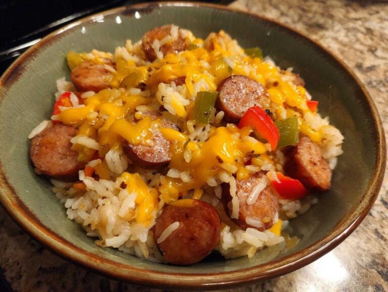 Close-up of cheesy sausage and rice mixed with bell peppers served in a rustic green bowl.