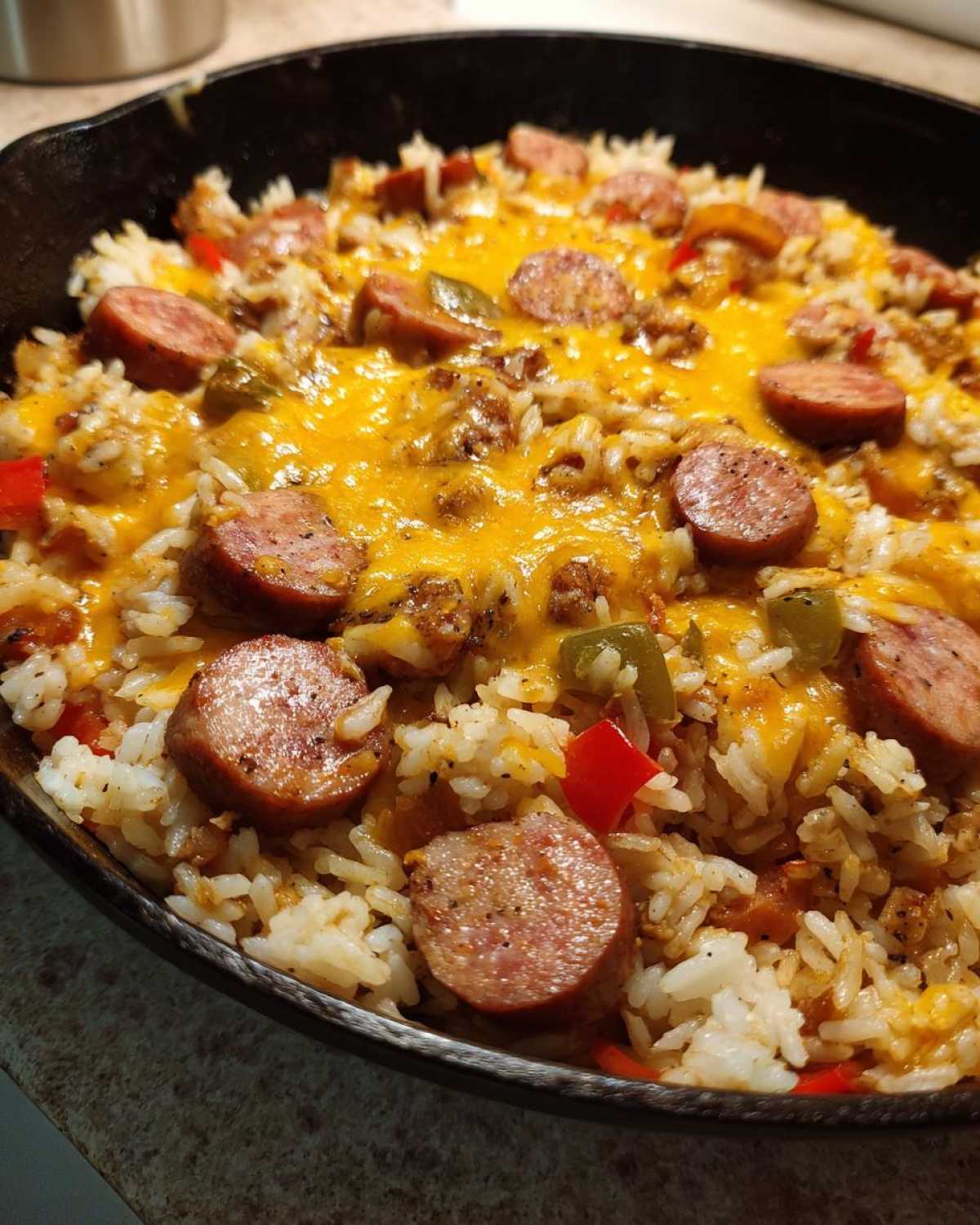 Close-up of cheesy sausage and rice casserole topped with melted cheddar cheese and sliced smoked sausage.