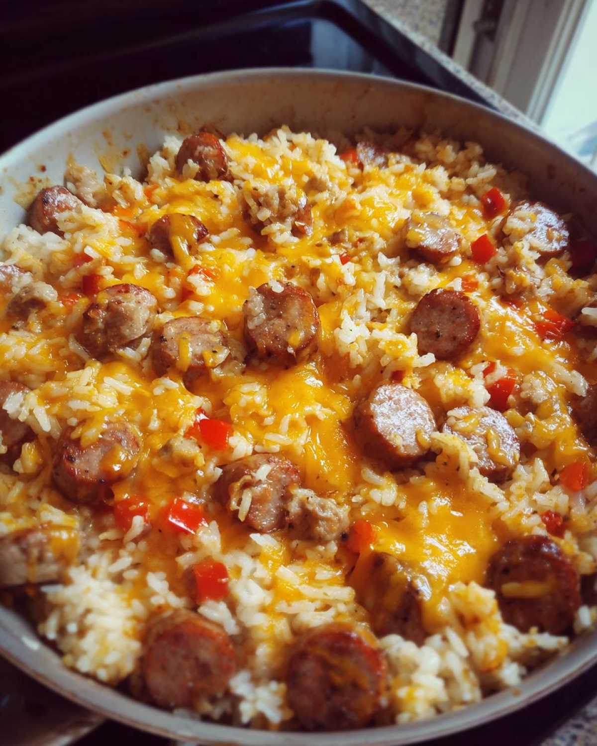 Close-up view of a skillet filled with cheesy sausage and rice mixed with red peppers.