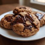 Close-up of four freshly baked chewy chocolate chip cookies with melted chocolate chunks on a white plate.