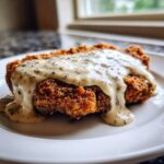 Close-up of a crispy, golden-brown chicken fried steak smothered in thick, peppered country gravy.