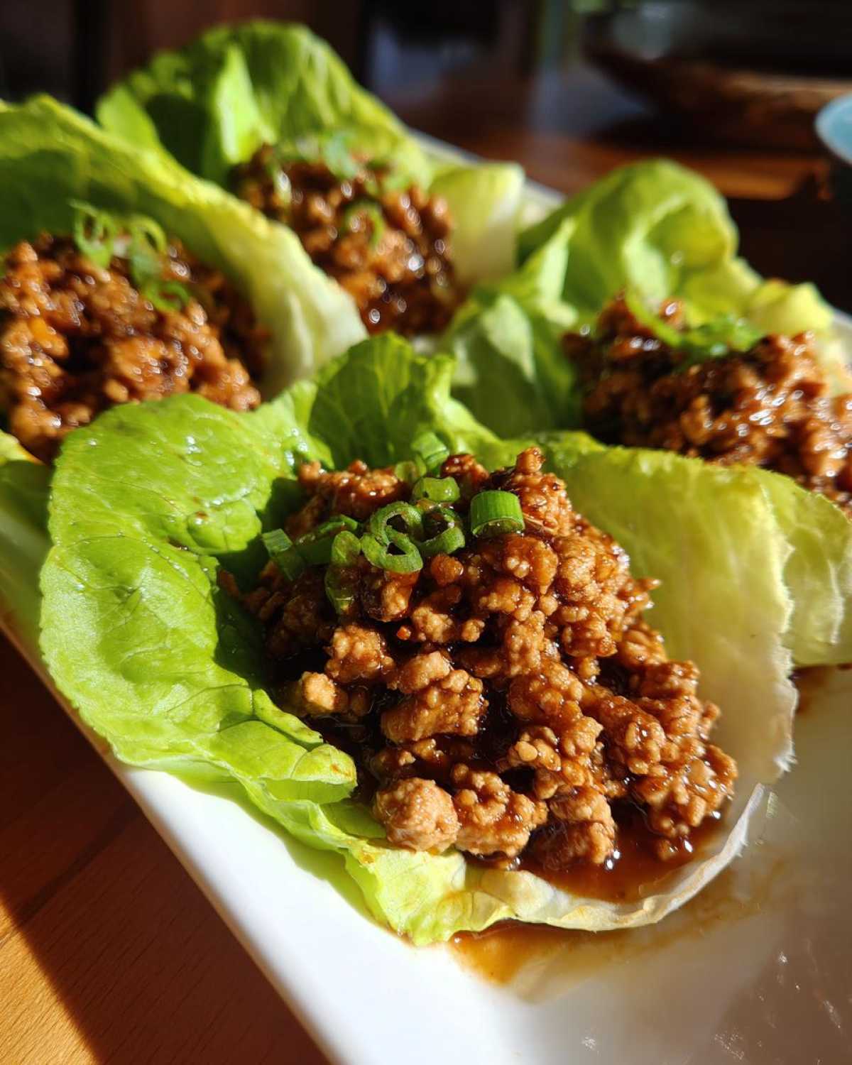 Close-up of savory ground chicken lettuce wraps topped with sliced green onions.