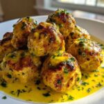 A plate of golden-brown chicken piccata meatballs smothered in a bright yellow lemon-caper sauce and garnished with parsley.