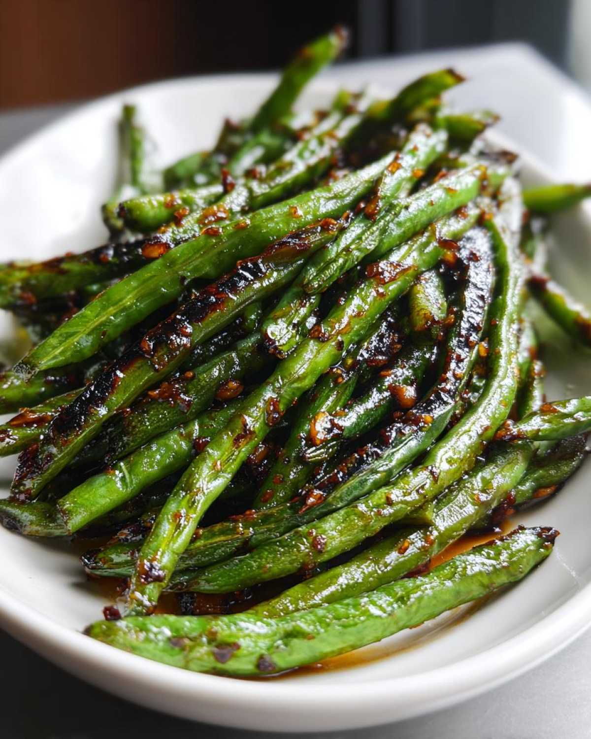 Close-up of vibrant green beans coated in a dark, glossy chinese green beans with garlic sauce.
