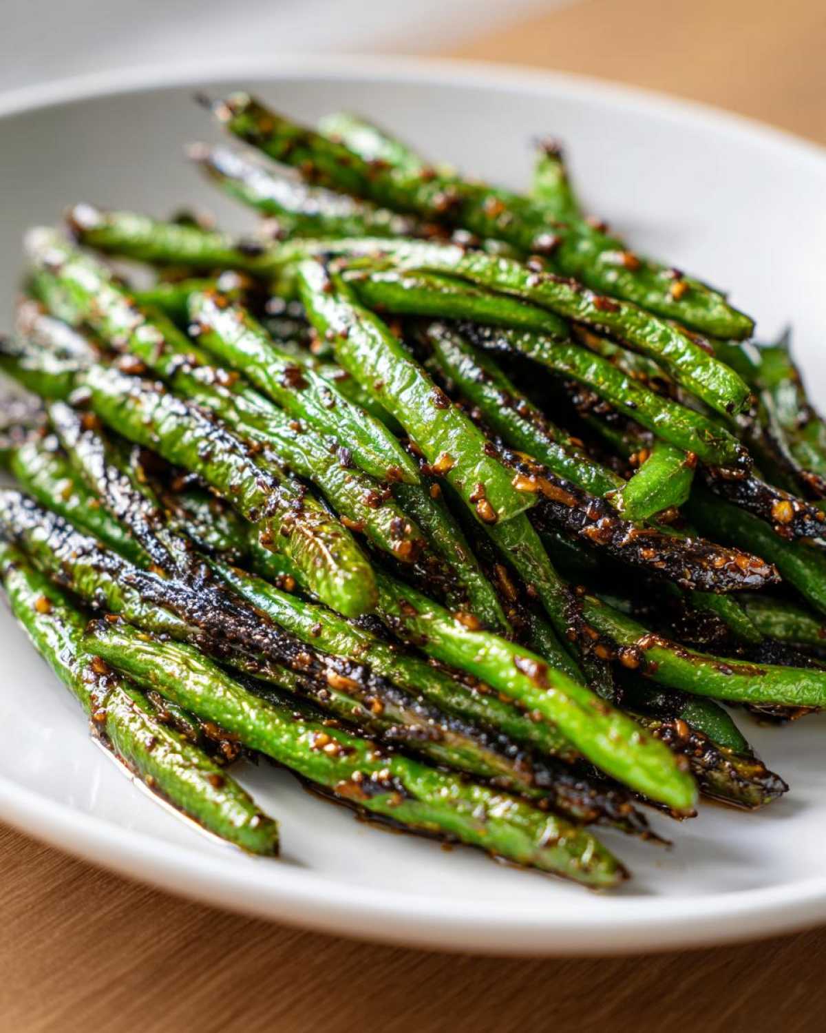A close-up shot of vibrant, blistered chinese green beans with garlic sauce piled on a white plate.