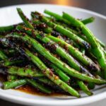 Close-up of vibrant green beans coated in a dark, savory chinese green beans with garlic sauce.