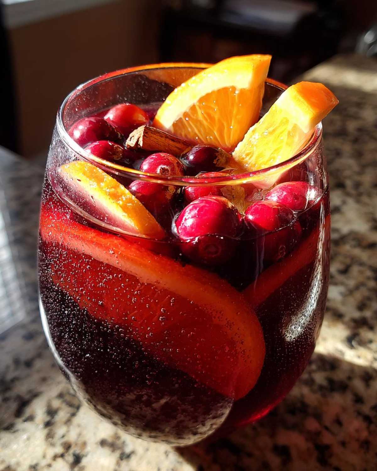 Close-up of a glass filled with sparkling Christmas sangria, garnished with fresh cranberries, orange slices, and a cinnamon stick.