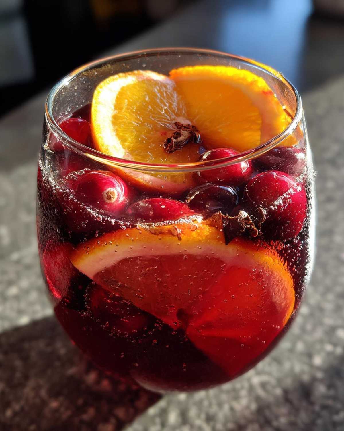 Close-up of a glass filled with bubbling Christmas sangria, garnished with orange slices, fresh cranberries, and cloves.