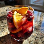 Close-up of a glass filled with chilled Christmas sangria, ice cubes, orange slices, and cranberries.