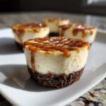 A close-up of a single cookie butter cheesecake cup topped with caramel drizzle, sitting on a white plate.