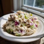 A scoop of creamy cottage cheese chicken salad mixed with diced red onion and celery served on a white plate.