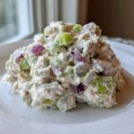 A mound of creamy cottage cheese chicken salad mixed with chunks of red onion and green celery on a white plate.