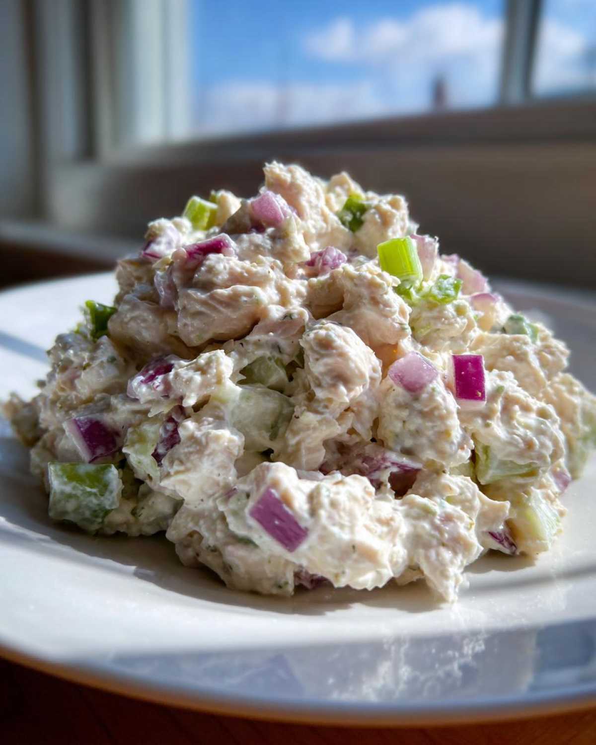 A close-up serving of creamy cottage cheese chicken salad mixed with diced red onion and celery.