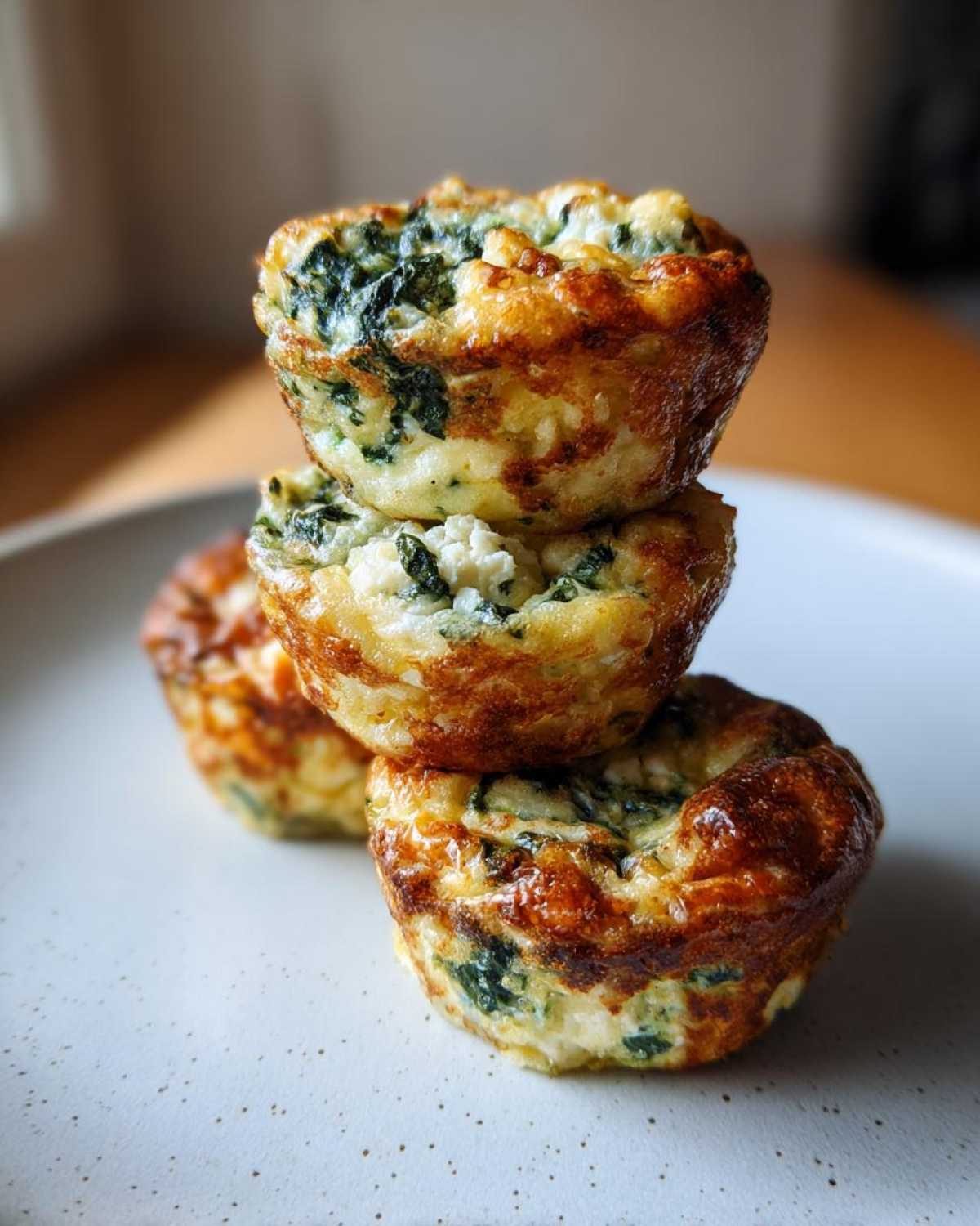Three golden-brown Cottage Cheese Egg Cups With Spinach & Feta stacked on a speckled plate.