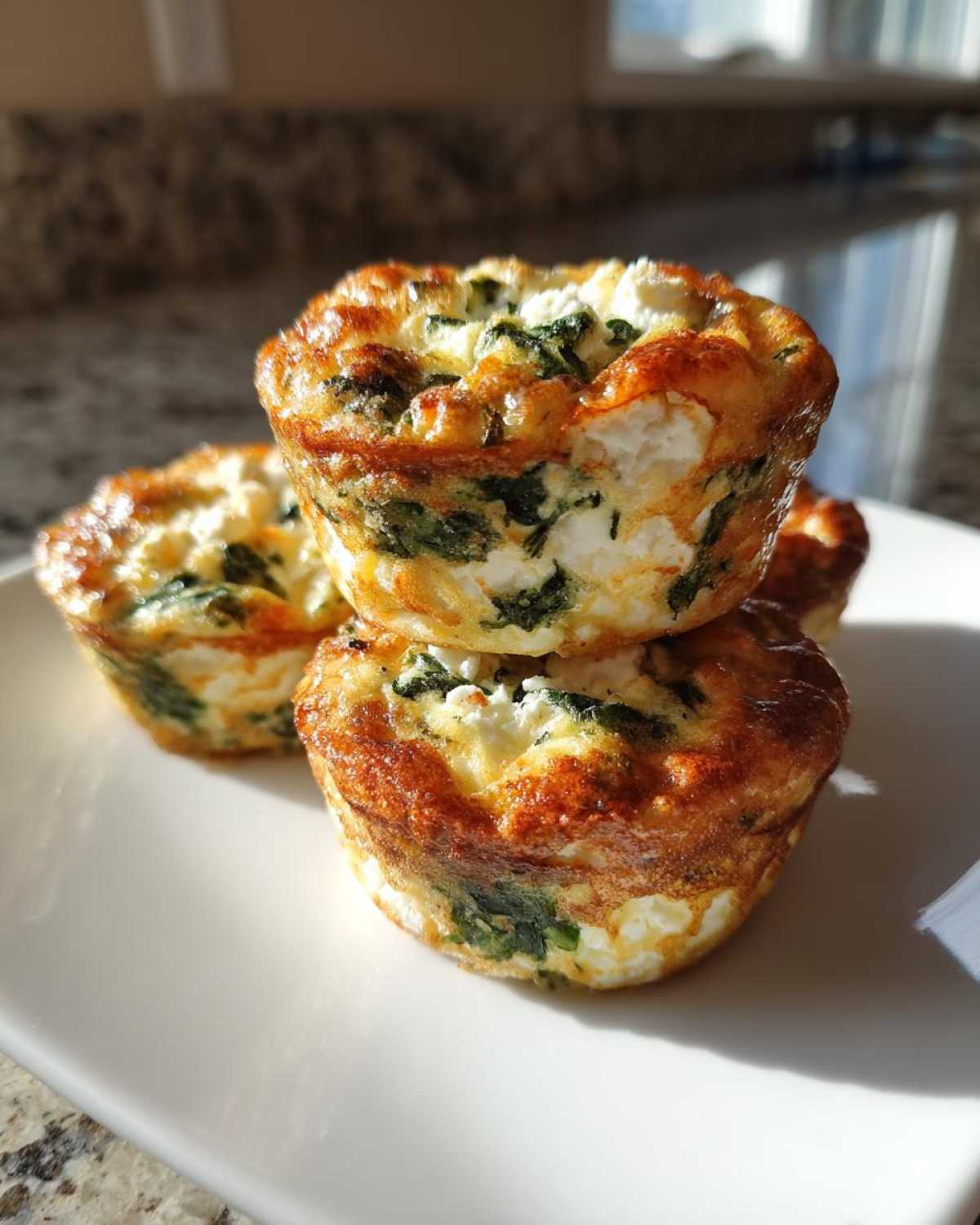 A stack of golden-brown Cottage Cheese Egg Cups With Spinach & Feta on a white plate.