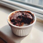 A rich, dark chocolate Cottage Cheese Microwave Brownie served warm in a white fluted ramekin, with a bite taken out.