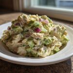 A mound of creamy avocado chicken salad mixed with chunks of avocado and red onion served on a white plate.