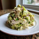 A mound of creamy avocado chicken salad featuring chunks of avocado, shredded chicken, and red onion on a white plate.