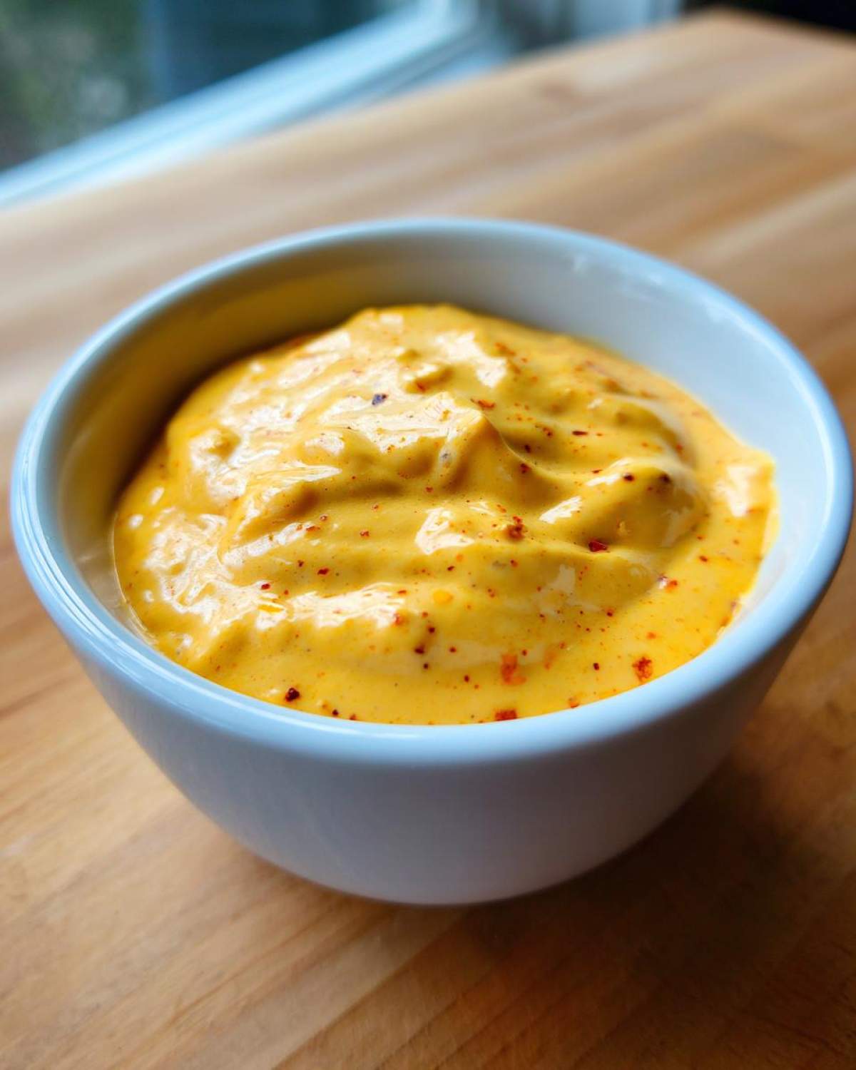 Close-up of thick, creamy, orange-yellow beer cheese dip sprinkled with red pepper flakes in a white bowl.