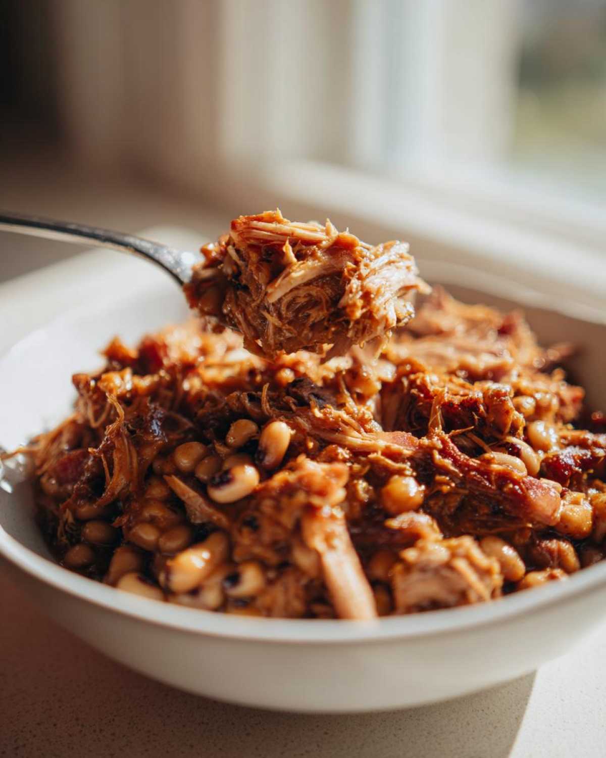 A fork lifting a bite of pulled pork over a bowl of creamy black eyed peas.