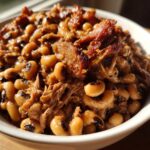 Close-up of creamy black eyed peas cooked with savory pulled smoked meat in a white bowl.