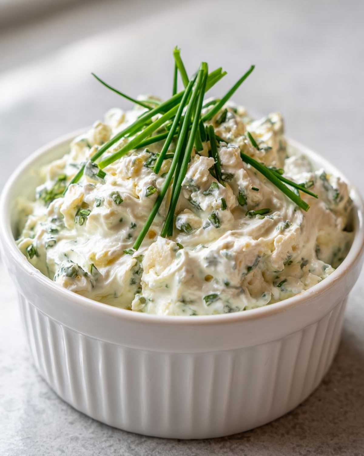 Close-up of a thick, creamy blue cheese dip mixed with herbs, garnished with whole chives.