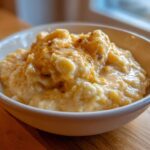 Close-up of a creamy bowl of rich, yellow cheese grits topped with melted butter or sauce.