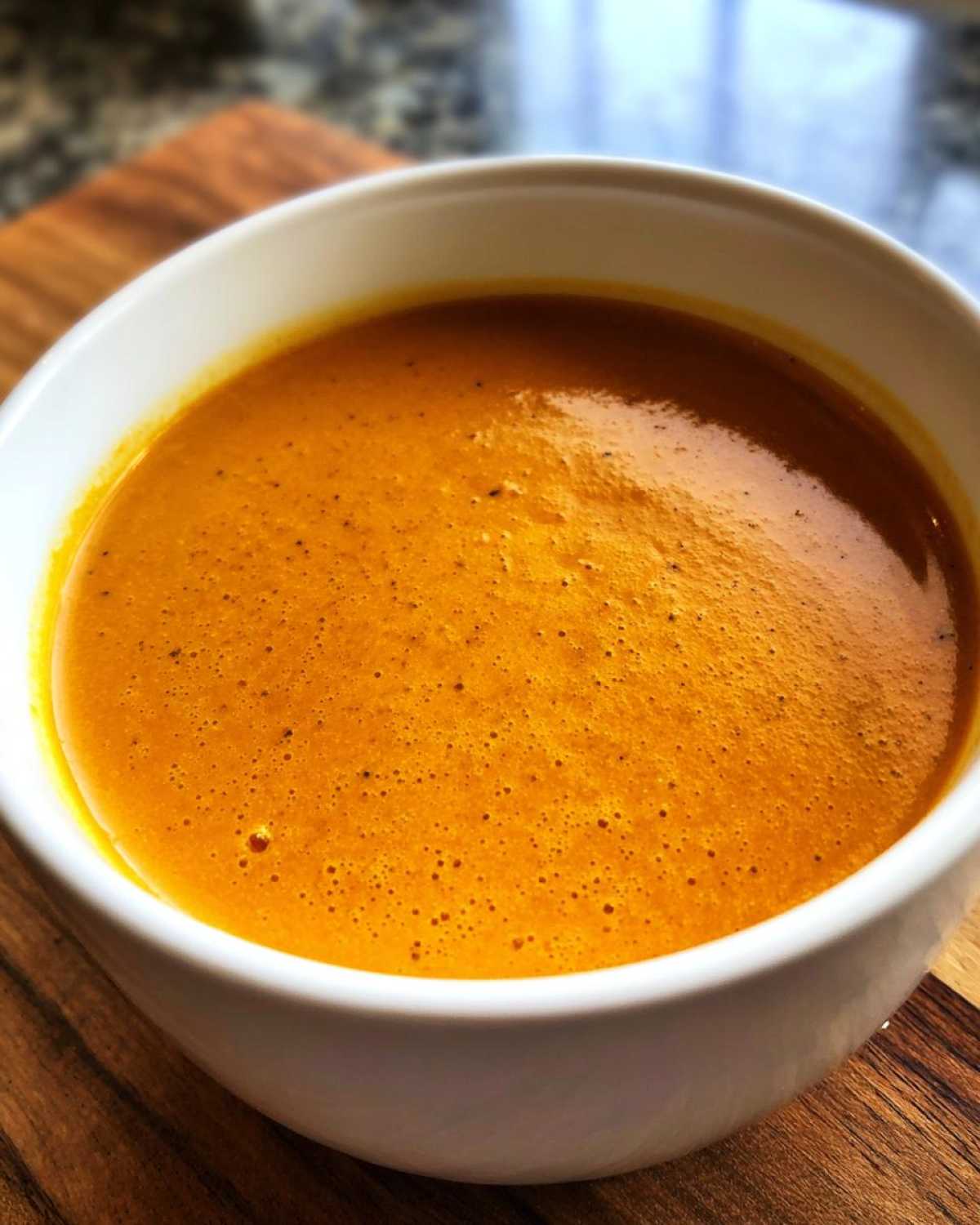 Close-up of a rich, creamy orange cheese soup with small bubbles on the surface, served in a white bowl.