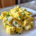 Close-up of a spoonful of creamy egg salad recipe garnished with chopped green onions.