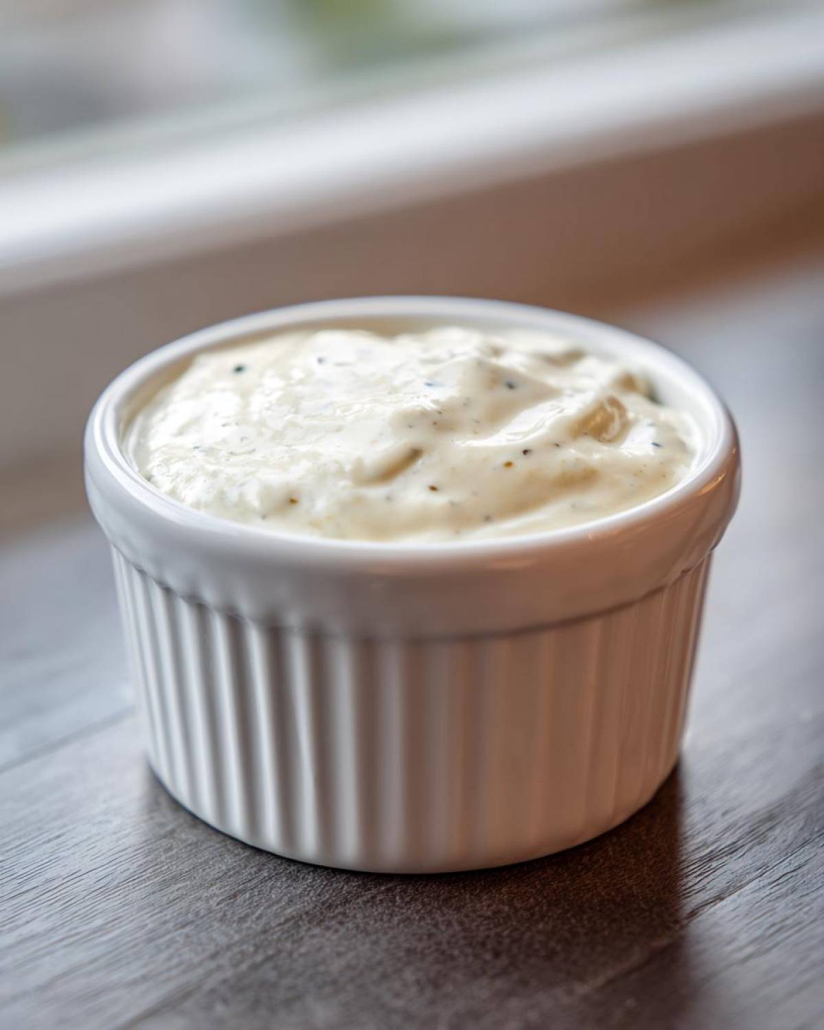 A small white ramekin filled with creamy horseradish sauce, sitting on a dark wooden surface.