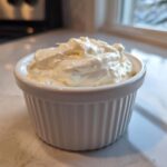 A small white ramekin filled high with fluffy, white creamy horseradish sauce, set on a light countertop.