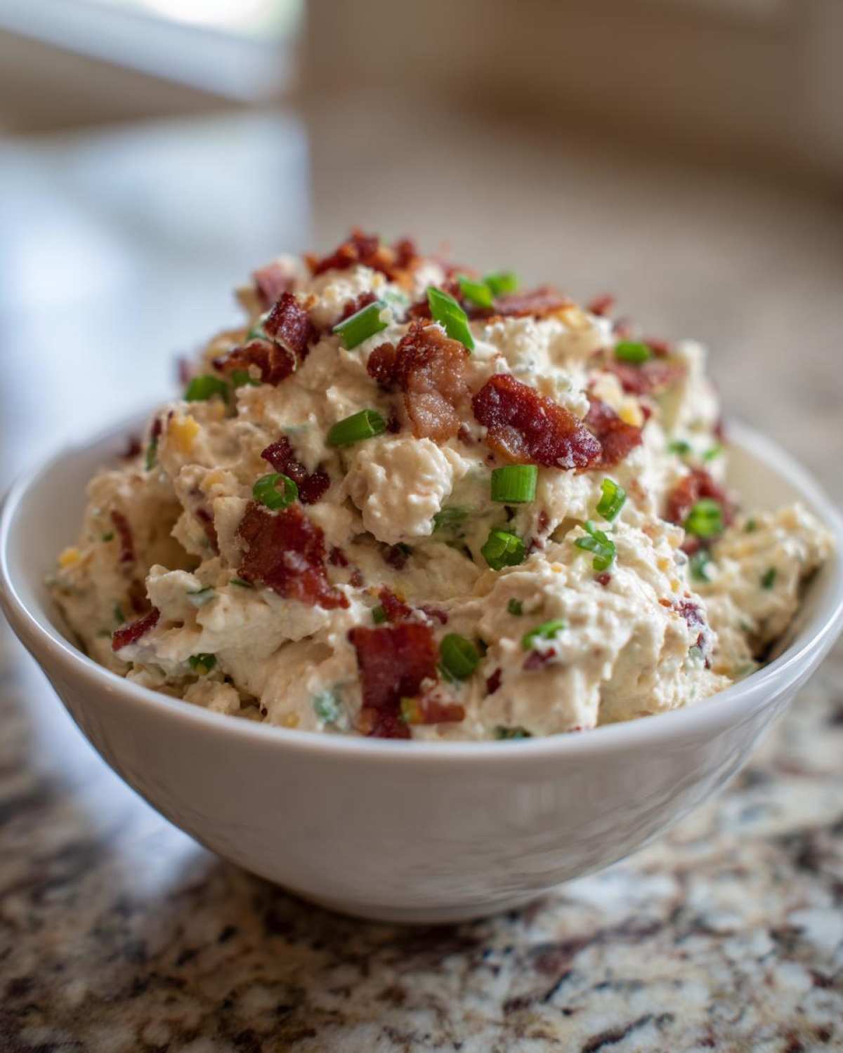 Close-up of creamy Million Dollar Dip topped generously with crispy bacon bits and fresh green onions.