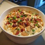A close-up of creamy Neiman Marcus dip topped generously with crumbled bacon, sliced almonds, and green onions.