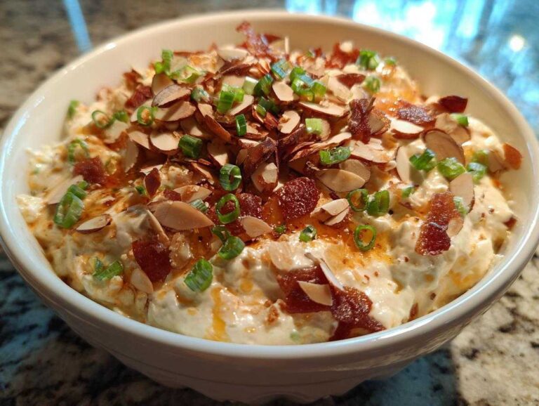 A bowl of creamy Neiman Marcus Dip topped generously with sliced almonds, crumbled bacon, and green onions.