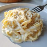 Close-up of fettuccine pasta generously coated in rich homemade alfredo sauce, topped with grated Parmesan and black pepper.