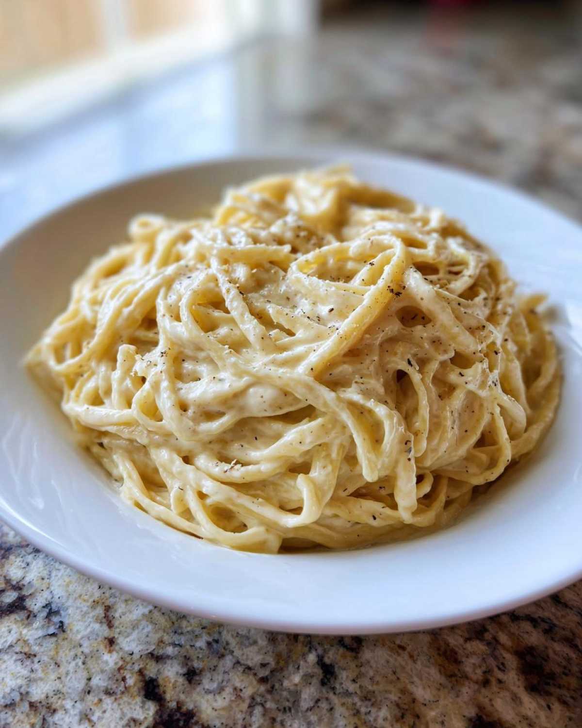 A close-up of fettuccine pasta generously coated in creamy Olive Garden Alfredo sauce and sprinkled with black pepper.